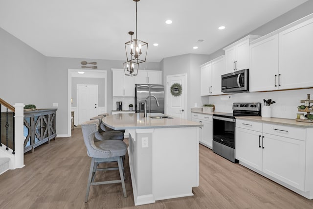 kitchen with a sink, light wood finished floors, appliances with stainless steel finishes, and a center island with sink