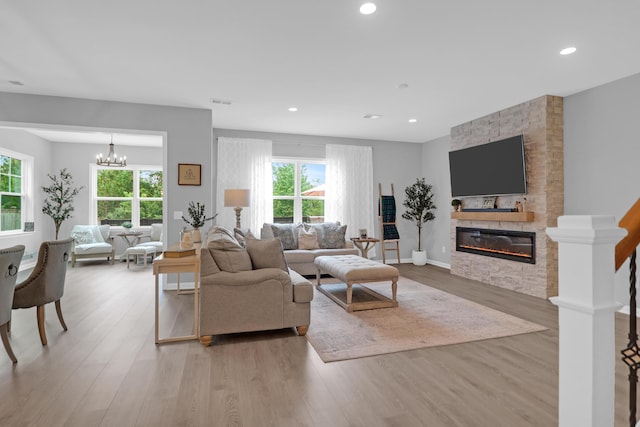 living area featuring light wood-style floors, an inviting chandelier, recessed lighting, and a stone fireplace
