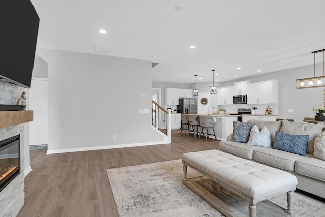 living room featuring recessed lighting, light wood-style floors, stairway, and a fireplace