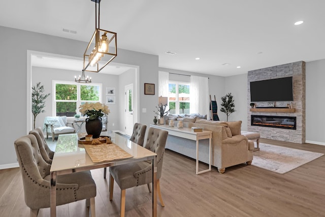 dining room with a chandelier, visible vents, a stone fireplace, and light wood-style flooring