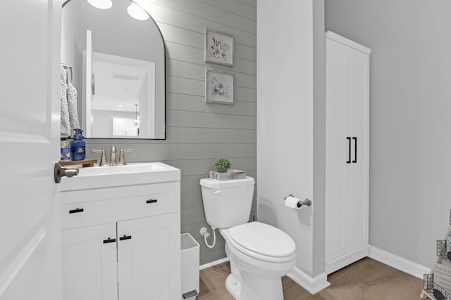 half bath with wooden walls, vanity, toilet, baseboards, and wood finished floors