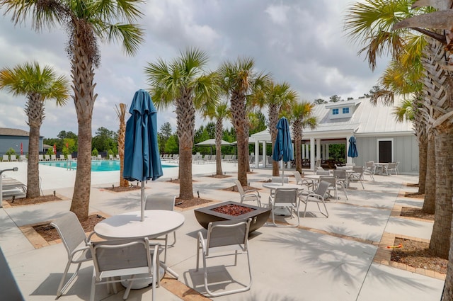 view of patio with a community pool, outdoor dining area, and an outdoor fire pit