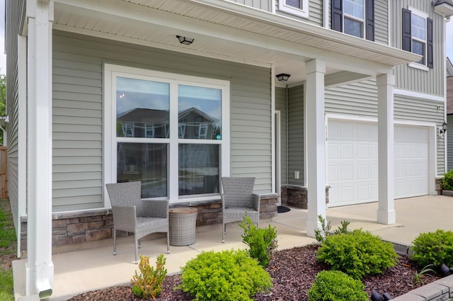 entrance to property featuring a porch, driveway, stone siding, and a garage