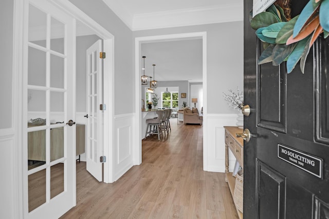 entryway featuring french doors, crown molding, light wood-type flooring, a wainscoted wall, and a decorative wall