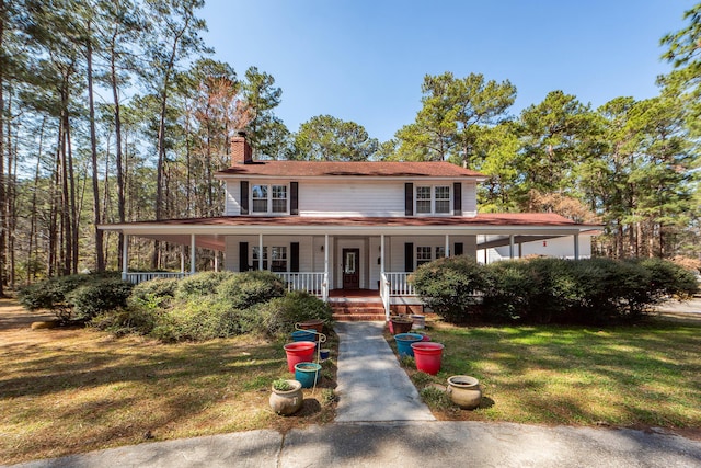 country-style home with a porch, a front yard, and a chimney