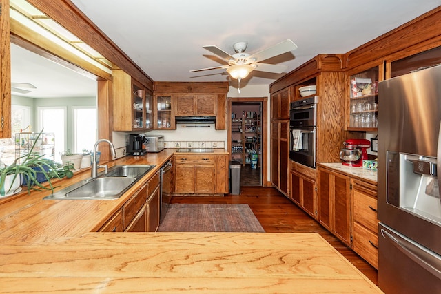 kitchen with glass insert cabinets, dark wood-style flooring, stainless steel appliances, a sink, and exhaust hood