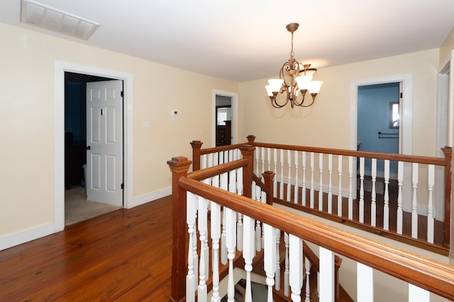 corridor featuring a chandelier, wood finished floors, an upstairs landing, visible vents, and baseboards