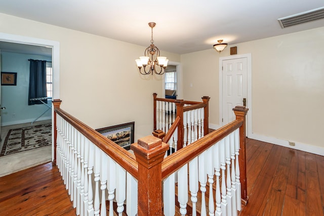 hallway with visible vents, hardwood / wood-style floors, an inviting chandelier, an upstairs landing, and baseboards