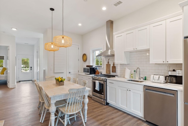 kitchen with visible vents, a sink, appliances with stainless steel finishes, wall chimney exhaust hood, and white cabinets