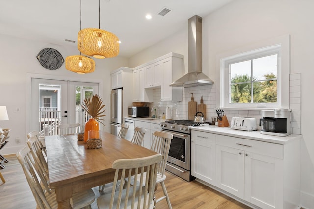 kitchen with high end appliances, light wood finished floors, a sink, wall chimney exhaust hood, and tasteful backsplash