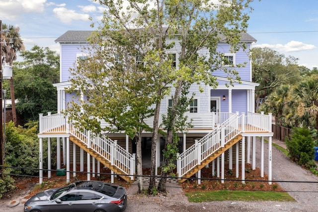 view of front facade with a porch, stairs, roof with shingles, and fence