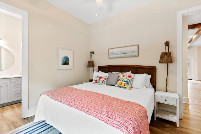 bedroom with ensuite bath, light wood-style flooring, and baseboards