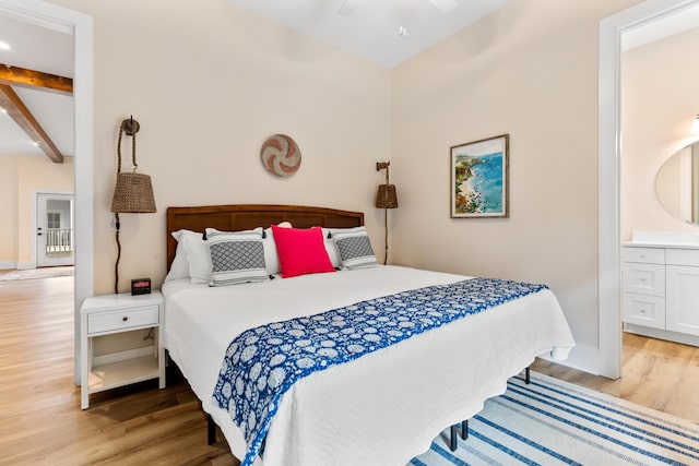 bedroom featuring beam ceiling, wood finished floors, baseboards, and connected bathroom