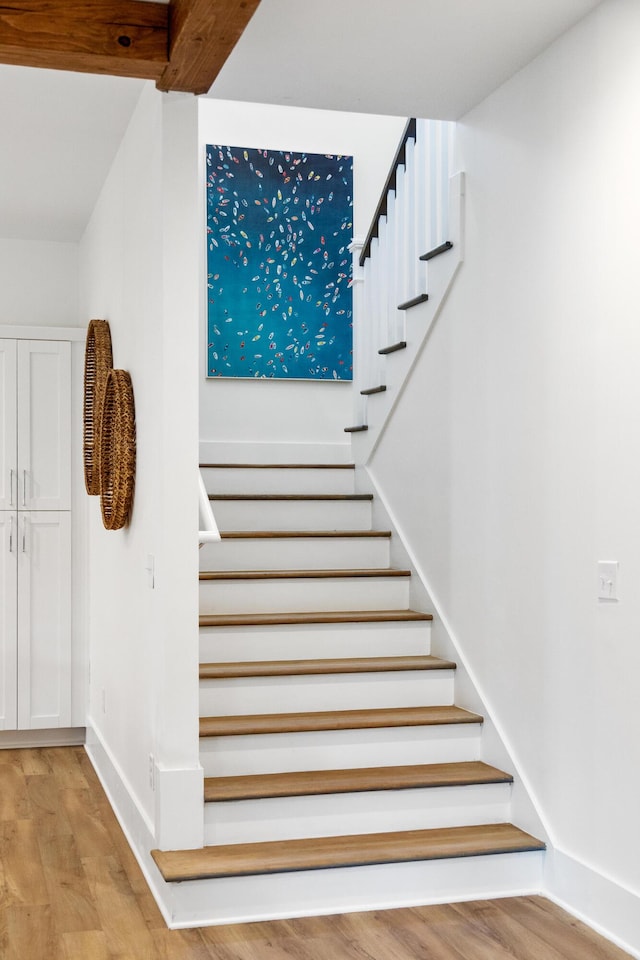 stairway featuring beamed ceiling, baseboards, and wood finished floors