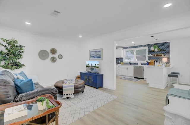 living area with ornamental molding, light wood-style flooring, and recessed lighting