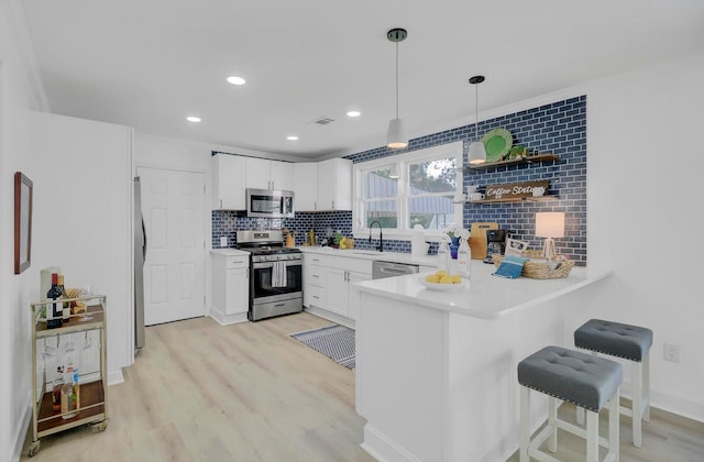 kitchen featuring a peninsula, a kitchen breakfast bar, light wood-style floors, appliances with stainless steel finishes, and tasteful backsplash