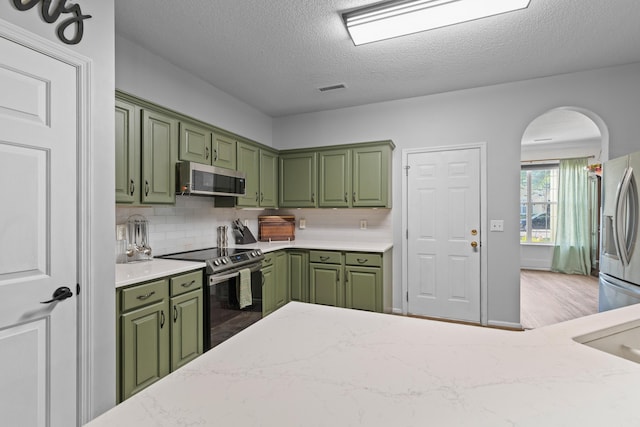 6242 Fieldstone Cir, Charleston, SC 29414 - kitchen with green cabinetry, stainless steel appliances, arched walkways, decorative backsplash, and light stone counters