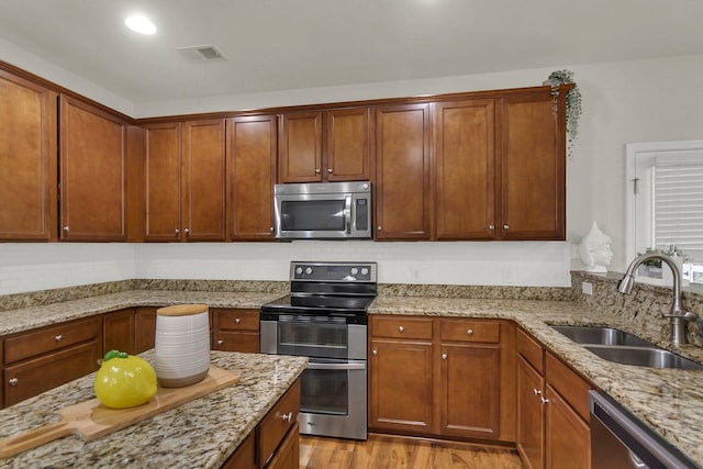 kitchen with light hardwood / wood-style floors, appliances with stainless steel finishes, sink, and light stone counters