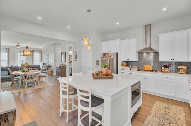 kitchen with pendant lighting, light wood-type flooring, stainless steel appliances, and wall chimney range hood