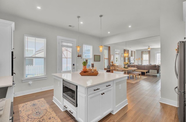 kitchen with pendant lighting, white cabinetry, stainless steel appliances, and hardwood / wood-style flooring