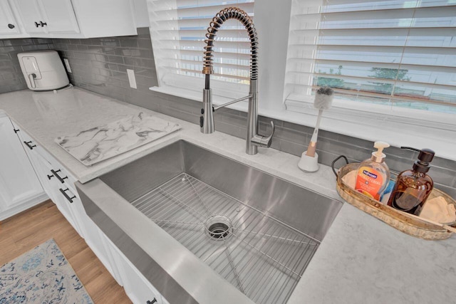 details featuring light stone countertops, sink, light hardwood / wood-style flooring, decorative backsplash, and white cabinets