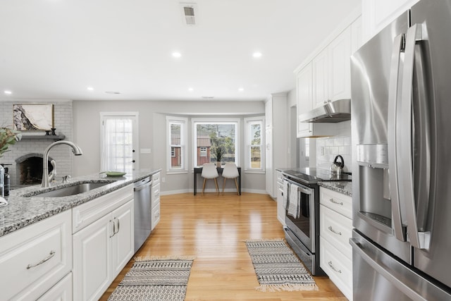 kitchen featuring a brick fireplace, under cabinet range hood, light wood-type flooring, appliances with stainless steel finishes, and a sink