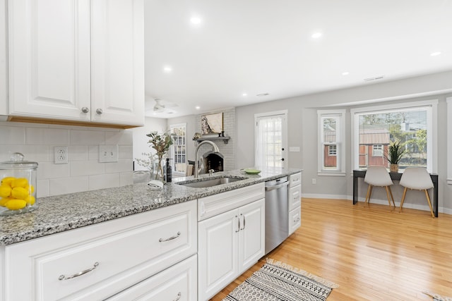 kitchen featuring a sink, backsplash, stainless steel dishwasher, white cabinetry, and a healthy amount of sunlight