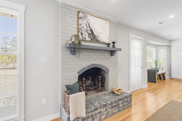 living area featuring visible vents, baseboards, a brick fireplace, and wood finished floors