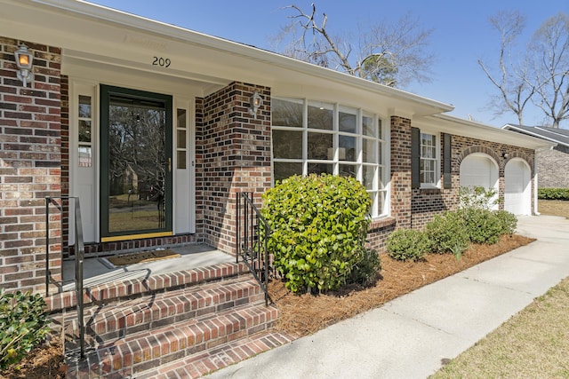 entrance to property featuring brick siding, concrete driveway, and a garage