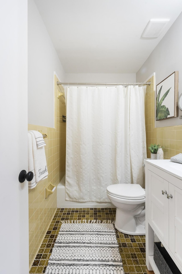 full bath featuring visible vents, toilet, shower / tub combo with curtain, tile walls, and vanity