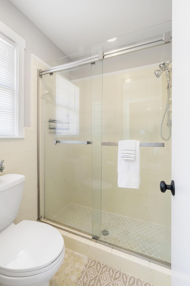 bathroom featuring toilet, tile walls, and a stall shower