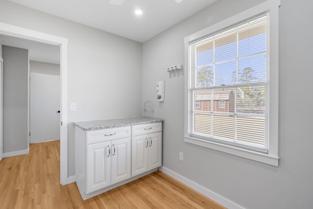 interior space with white cabinets, light wood-type flooring, baseboards, and light stone countertops