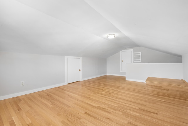 bonus room with baseboards, light wood-style flooring, and vaulted ceiling