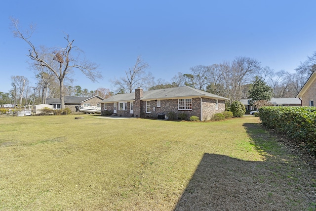 rear view of house featuring a yard, brick siding, and a chimney