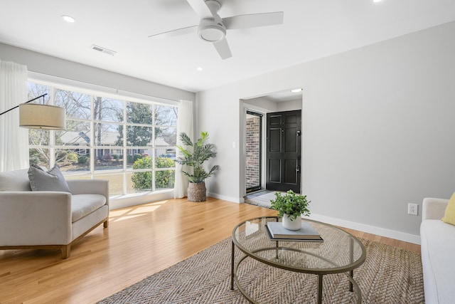 living area with visible vents, baseboards, light wood-style flooring, and a ceiling fan