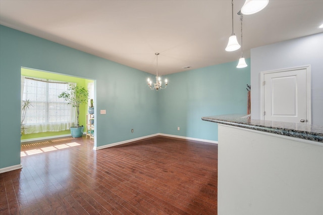 unfurnished dining area featuring a notable chandelier, dark wood finished floors, and baseboards