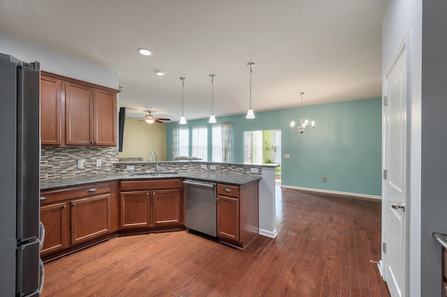 kitchen with decorative backsplash, appliances with stainless steel finishes, brown cabinetry, a sink, and a peninsula