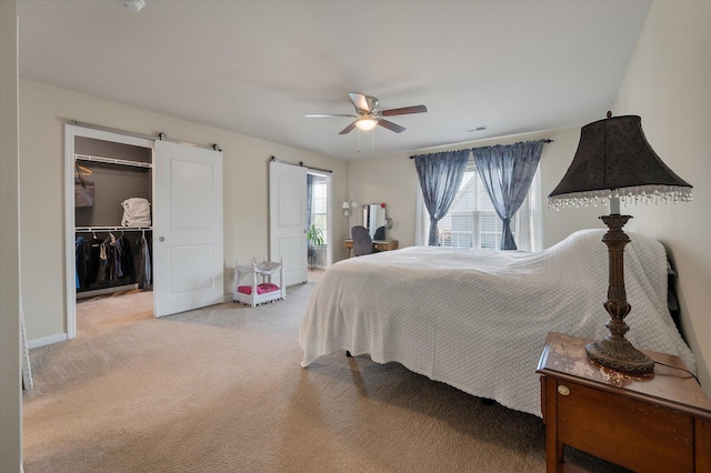 bedroom featuring a barn door, light colored carpet, a ceiling fan, visible vents, and a walk in closet