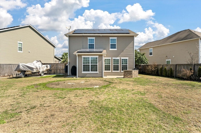 rear view of house featuring a fenced backyard, a yard, and solar panels