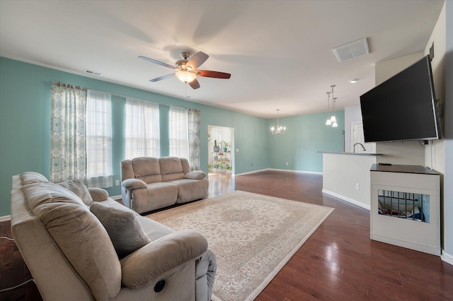 living room featuring dark wood-style floors, visible vents, baseboards, and ceiling fan with notable chandelier