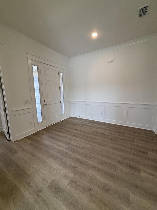 entryway with dark wood-style floors, visible vents, a decorative wall, and ornamental molding