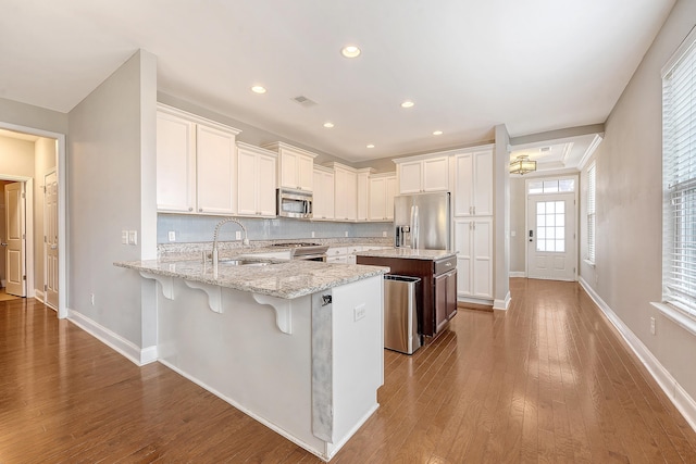 kitchen featuring appliances with stainless steel finishes, a sink, a peninsula, baseboards, and recessed lighting