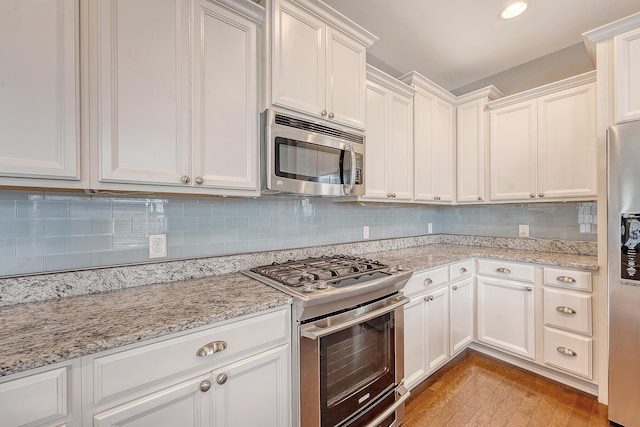 kitchen featuring appliances with stainless steel finishes, white cabinetry, backsplash, and light stone countertops