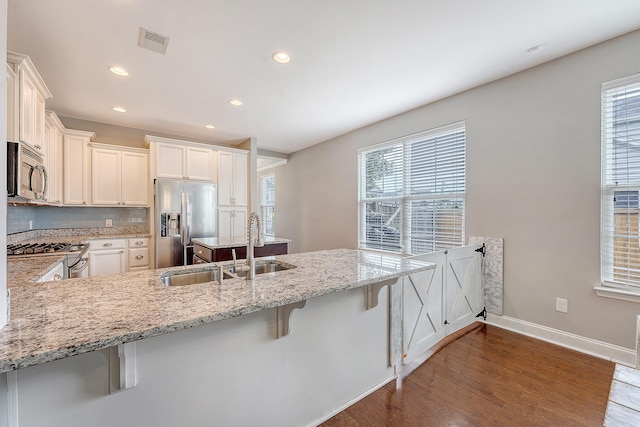 kitchen with stainless steel appliances, a sink, light stone countertops, hardwood / wood-style flooring, and baseboards