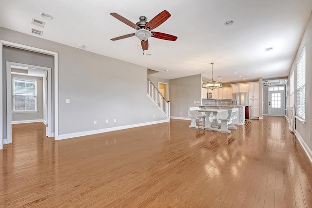 unfurnished living room with baseboards, ceiling fan, light wood-type flooring, stairway, and a chandelier