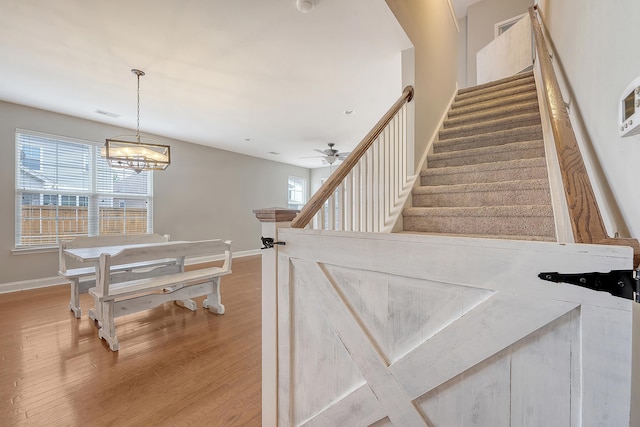 staircase featuring baseboards, wood finished floors, a ceiling fan, and a chandelier
