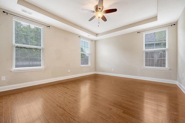 unfurnished room featuring wood finished floors, baseboards, ceiling fan, and a tray ceiling