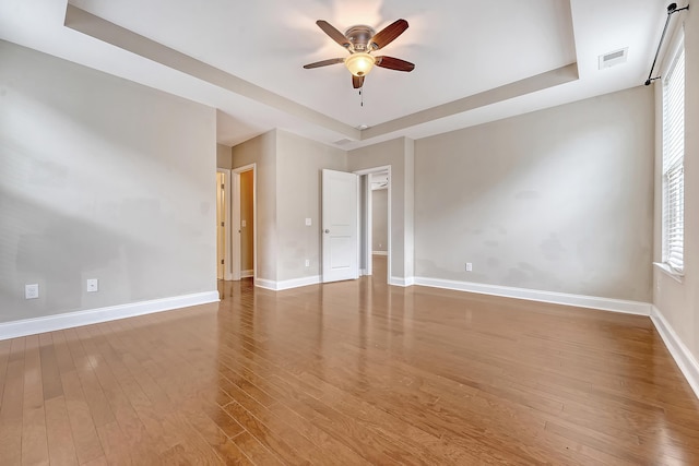 unfurnished room with a tray ceiling, a ceiling fan, baseboards, and wood finished floors