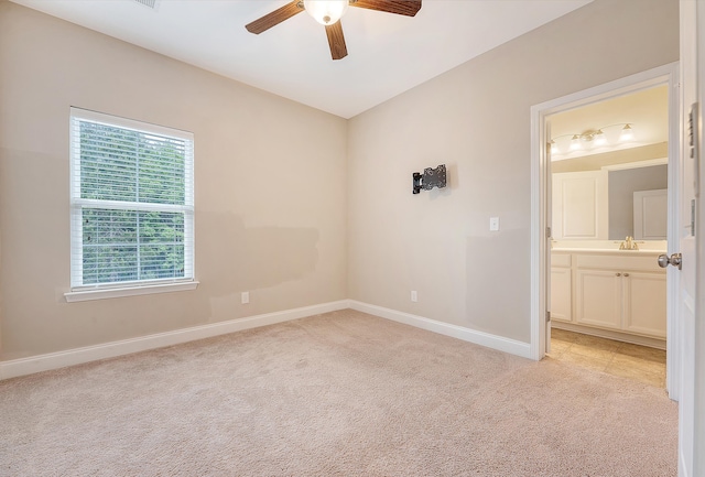 unfurnished bedroom with light carpet, baseboards, a sink, ceiling fan, and connected bathroom