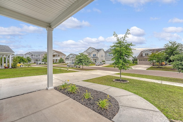 view of grassy yard featuring a residential view, concrete driveway, and a garage